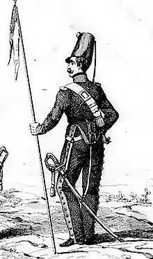 Un soldat de dos, la tête tourné vers la gauche, tenant une lance de sa main gauche.