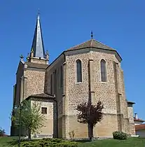 Une église derrière des petits arbres dont le clocher est en arrière-plan à gauche et le chœur en premier plan à droite.