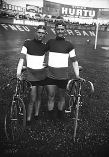 Photographie noir et blanc de deux cyclistes à l'arrêt avec leurs machines.