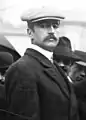 Photographie noir et blanc en buste d'un civil en costume portant une casquette.