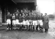 Des joueurs de rugby en tenue et des hommes en manteaux posent en rang pour une photo de groupe