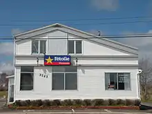 Photographie d'un bâtiment de Tracadie-Sheila abritant, entre autres, des locaux du journal L'Étoile. Sur l'affiche apparaît le log, aux couleurs du drapeau de l'Acadie.