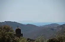 Photographie montrant l'île d'Asinara (Sardaigne) au fond d'une vallée vue depuis Cognocoli, avec le clocher de l’église au premier plan