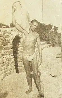 Photographie noir et blanc. Homme en maillot de bain portant sur son épaule une amphore.