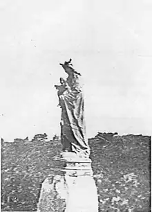 Photographie noir et blanc d'une statue en bronze. Une femme drapée en pieds couronnée porte un enfant.