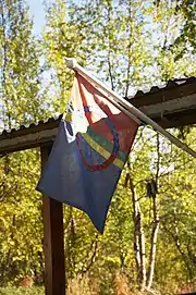 Un drapeau rouge et bleu orné de motifs multicolores accroché sur une habitation, avec des arbres en arrière-plan.