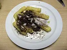 Dans une assiette blanche, quenelles de pommes de terre nappées de sucre fondant et de graines de pavot.