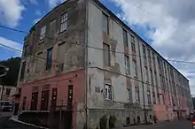 Photographie en couleurs d'un bâtiment longiligne de quatre niveaux, à la façade décrépie.