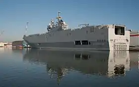 Un long navire militaire, à l'aspect légèrement similaire à celui d'un ferry, mouillant dans un port.