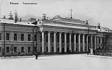 Photographie en noir et blanc d'un imposant bâtiment avec une façade à colonnades sous la neige.