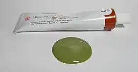 Sur un plan horizontal, un tube de pommade blanc et quelques millilitres de son contenu, de couleur vert argile.