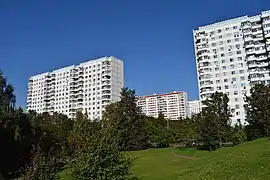 Des barres d'immeubles ; à l'avant-plan, une pelouse verte et arborée.