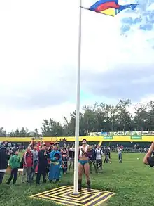 Photographie d'un lutteur en slip hissant un drapeau, entouré d'une foule bigarrée dans un stade.