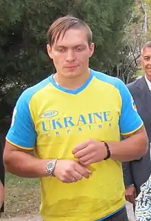 Photographie d'un homme debout habillé d'un T-shirt bleu et jaune, regardant vers le bas.