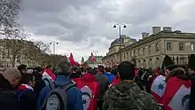 Foule de dos, portant des drapeaux, en milieu urbain.