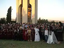 Photographie d'une foule vêtu de costumes traditionnels géorgiens devant un monument.