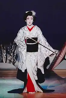 Photo couleur d'un homme travesti en femme, il porte une robe traditionnelle japonaise blanche et noire et tient dans ses mains un parapluie.
