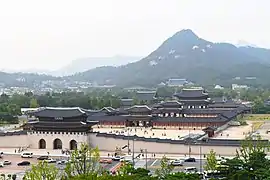 Photographie d'un palais vu de loin, quelques bâtiments sont visibles, et au loin une montagne domine l'ensemble.