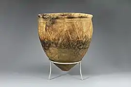 Photographie d'une poterie en forme de bol, présentant des motifs décoratifs sur les bords, posée sur un présentoir dans un musée.