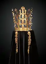 Couronne faite de bandeaux en or en forme d'arbres dressés aux feuilles d'or et pendentifs de jade (en forme de virgule). Photographie de face, sur fond sombre, la couronne étant posée sur un velours noir.