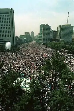 photographie d'une foule immense dans une vaste place bordée de quelques tours modernes.
