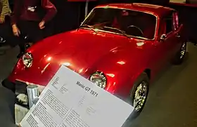 Une petite voiture rouge dans une salle d'exposition. Au premier plan, un écriteau où il est inscrit « Manic GT 1971 ».