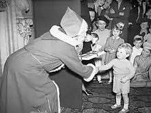 Le 17 décembre 1942, Winston Churchill Jr. (au premier plan à droite), à l'époque âgé de deux ans, reçoit des mains du Père Noël un livre de nursery rhymes lors de l'arbre de Noël de l'Amirauté, à Londres. Son grand-père Winston Churchill est alors Premier ministre du Royaume-Uni.