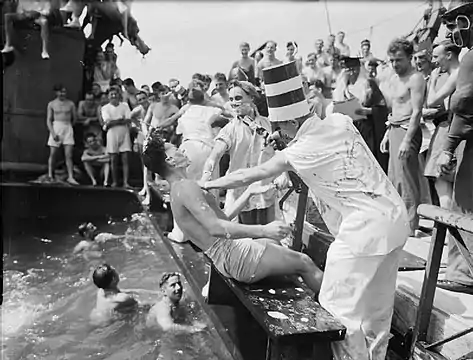 Dans la Royal Navy, en août 1941, cérémonie de passage de la ligne à bord du transport de troupes SS Empress of Australia (en) participant à un convoi de troupes africaines. Les initiés sont jetés à l'eau par les « ours », après avoir été rasés par le barbier du roi Neptune.