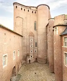 La photographie couleur montre une cour du palais de la Berbie. Les tours et les murailles en brique rouge paraissent immenses en comparaison avec les ouvertures.