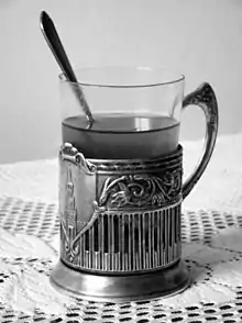Photo en noir et blanc d’un podstakannik en métal aec son verre plein d’une boisson chaude.