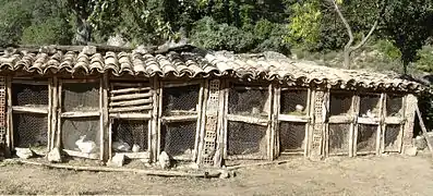 Série de clapiers extérieurs à 2 étages en briques et bois, portes en grillage à poules fermées par un loquet de métal et coincées en bas par une grosse pierre, couverture de tuiles romaines.