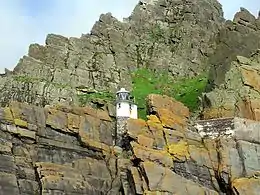 Photographie en couleurs d'un phare blanc entouré d'un escarpement rocheux.