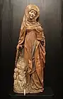 Photographie d'une statue de sainte en bois polychrome, représentant sainte Marthe enveloppée d'un manteau qui couvre des pénitents groupés à ses pieds