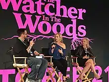 Trois personnes sur des chaises de réalisateur avec des micros devant le nom anglais du film en rose.
