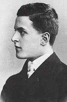 Portrait photographique en noir et blanc d'un jeune homme aux cheveux bruns coupés courts, tourné de profil et semblant amusé.
