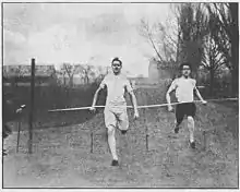 Photo en noir et blanc. Deux coureurs coupent la ligne d'arrivée. Les couloirs sont délimités par des cordes.