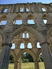Photographie des ruines de deux murs largement échancrés d'arcades et de fenêtres, situé l'un derrière l'autre.