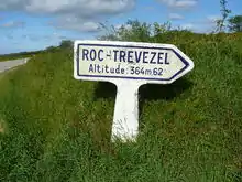 Panneau blanc en béton indiquant en lettres bleues « Roc'h Trevezel » et « Altitude 364m62 ». Le panneau est dans un décor herbeux, une route est légèrement visible à gauche.