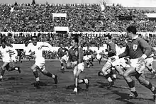 Photographie en noir et blanc d'un match de rugby opposant l'Italie en maillots blancs et la France en maillots sombres.