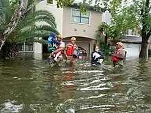 Trois militaires en gilets de sauvetage secourent un enfant et une femme dans une rue inondée.
