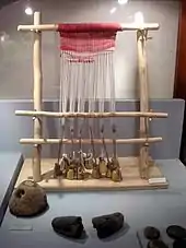 Photographie d'un métier à tisser vertical à pesons et à une barre de lisses, exposé dans la vitrine d'un musée.