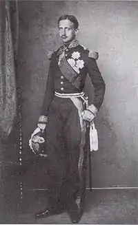 Photo en noir et blanc d'un jeune homme dans un uniforme militaire à col et épaulettes et portant un chapeau dans sa main.