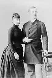 Photographie en noir et blanc d'une jeune femme portant une robe noire et d'un jeune homme en redingote.