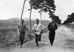 Trois hommes en habits amples et en pleine course sur une route de campagne.