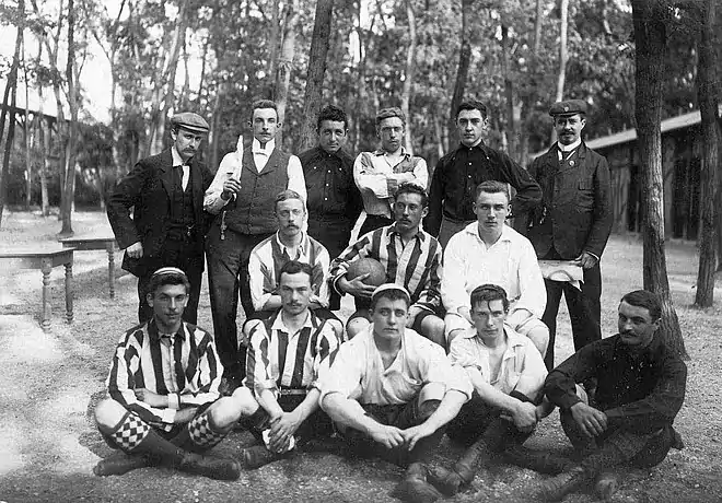 Photo en noir et blanc d'hommes sur trois rangs, trois portent un maillot et un au centre tient un ballon de football