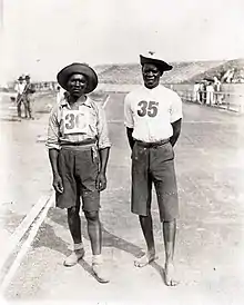 Deux hommes noirs, l'un pieds nus, posent sur une piste d'athlétisme.