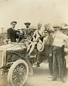 Un homme en sueur occupe une voiture, il est entouré de nombreux autres hommes qui posent avec lui.