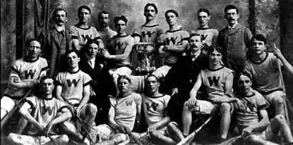 Photographie en noir et blanc d'une équipe posant fièrement autour d'un trophée, les maillots sont marqués d'un W