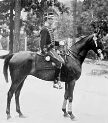 Photo en noir et blanc d'un cavalier en uniforme sur son cheval monté en bride présentant son profil droit.