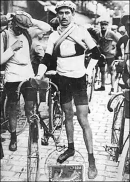 Photographie en noir et blanc d'un cycliste debut tenant son vélo de la main droite, au départ d'une course.